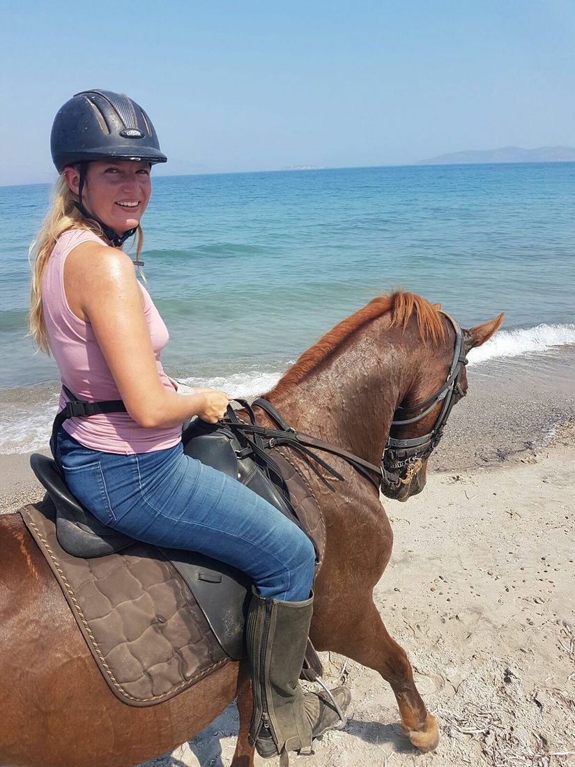 Nathalie Sameli mit Reithelm auf einem Pferd am Meer