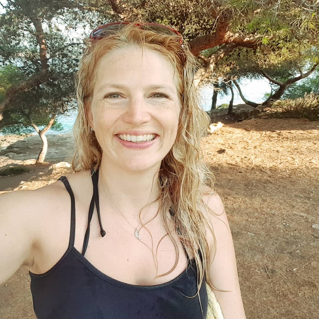 Nathalie Sameli im schwarzen Top unter Bäumen am Meer